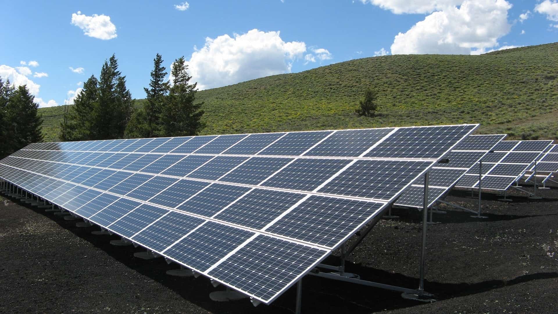 Array of solar panels in front of green hills and blue sky