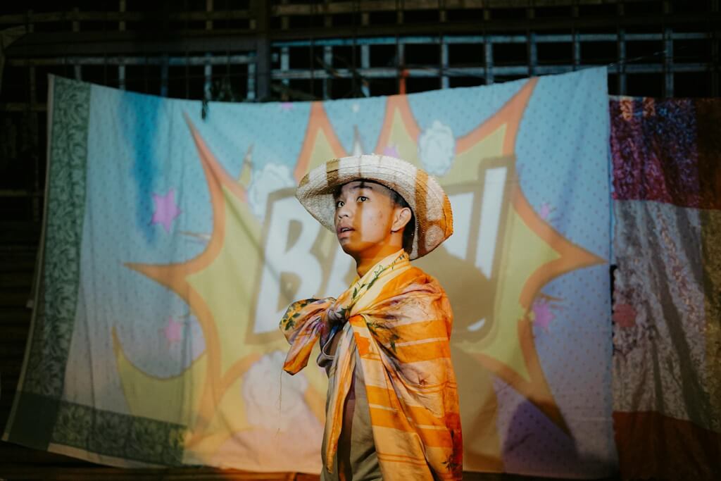Young boy in cowboy hat standing in front of flag that says bam